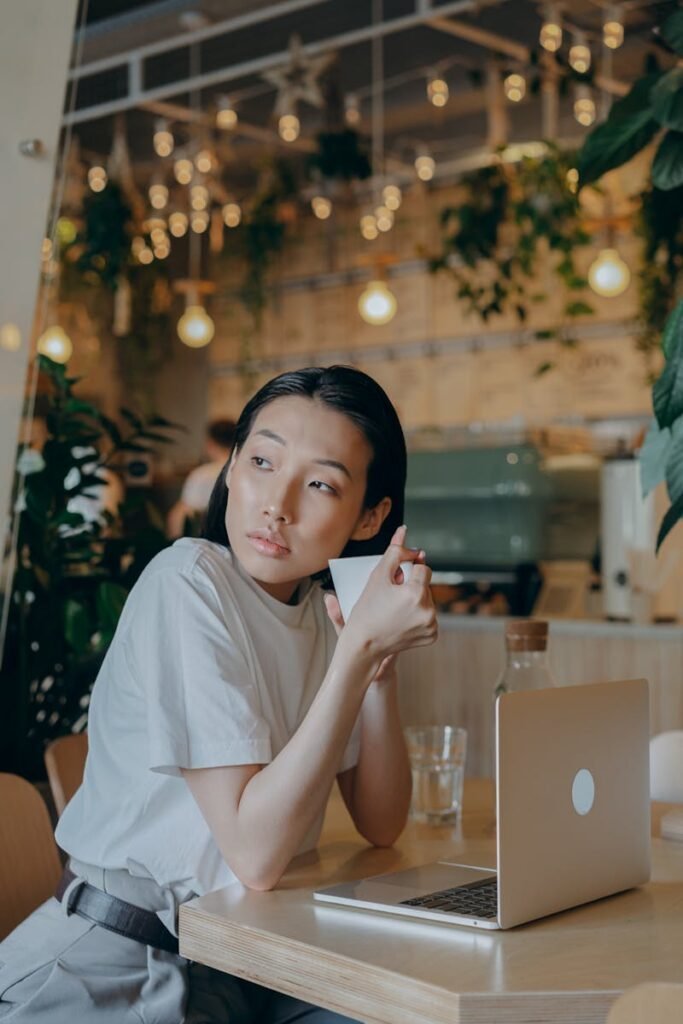 Asian businesswoman with laptop and cup in cozy cafe environment, highlighting remote work lifestyle.